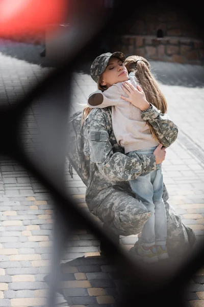 Daughter embracing mother in military uniform with blurred net on foreground, monochrome — Stock Photo