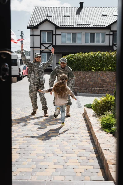 Daughter running to happy father and mother in military uniforms on street near house on blurred foreground — Stock Photo