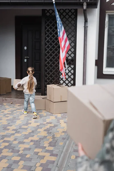 Menina carregando caixa de papelão para casa em primeiro plano borrado — Fotografia de Stock