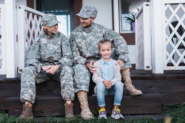 Smiling military father and mother with daughter sitting on house threshold — Stock Photo
