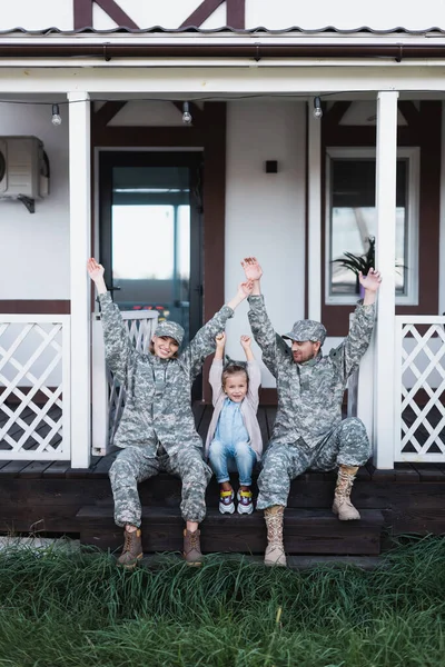 Happy family with hands in air sitting on house threshold on backyard — Stock Photo