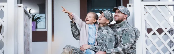 Happy military mother and father sitting near daughter pointing with finger, on backyard, banner — Stock Photo