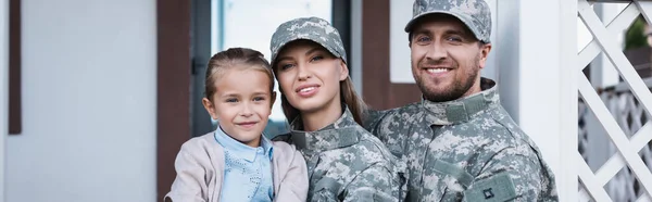 Portrait of smiling military mother and father with daughter looking at camera with house on background, banner — Stock Photo