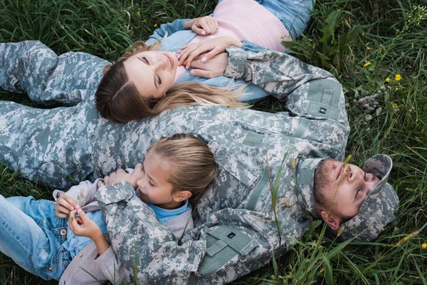 Overhead view of military serviceman resting and embracing wife and daughter, while lying on grass — Stock Photo