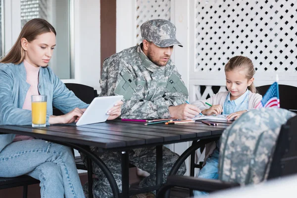 Military serviceman sitting near girl drawing and woman using digital tablet at home — Stock Photo