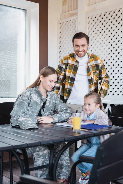 Glückliche Eltern sitzen neben Tochter und schreiben zu Hause am Notizbuch — Stockfoto