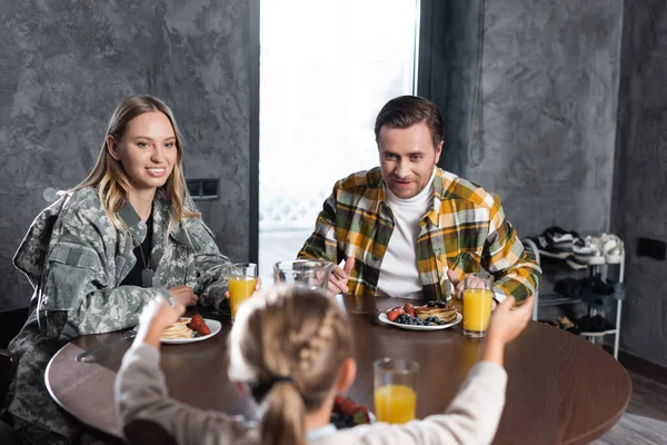 Pareja sonriente desayunando, sentada a la mesa en la cocina con una chica borrosa en primer plano - foto de stock