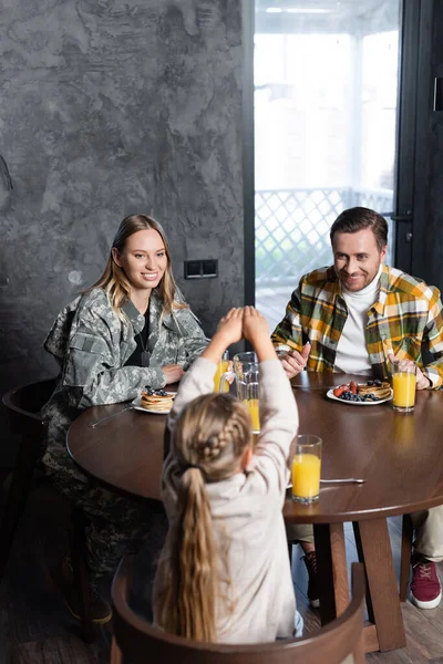 Улыбающаяся пара и дочь завтракают, сидя за столом на кухне — стоковое фото