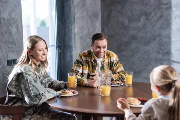 Coppia felice che fa colazione, ride, mentre si siede a tavola in cucina con ragazza sfocata in primo piano — Foto stock