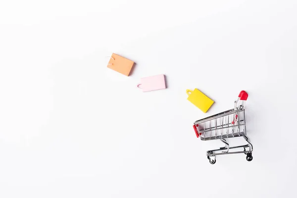 Vista superior de pequenos sacos de compras e carrinho no fundo branco — Fotografia de Stock