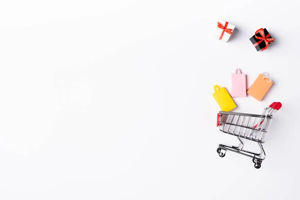 Vue du dessus des petites boîtes-cadeaux et des sacs à provisions près du chariot sur fond blanc — Photo de stock