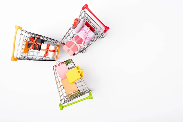 Vista superior de bolsas de compras de juguetes y regalos en carritos sobre fondo blanco - foto de stock
