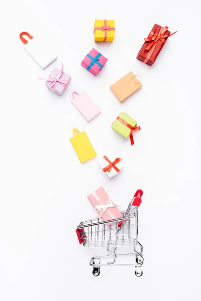 Vista superior de pequeños regalos y bolsas de compras cerca del carrito sobre fondo blanco - foto de stock