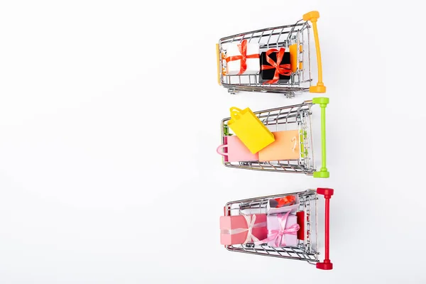 Top view of colorful shopping bags and toy gifts in carts on white background — Stock Photo