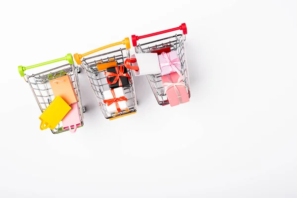 Top view of small shopping carts with gifts and bags on white background — Stock Photo