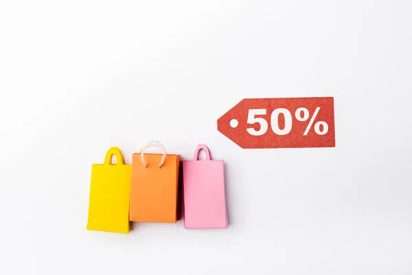 Top view of price tag with 50 percent signs near toy shopping bags on white background — Stock Photo
