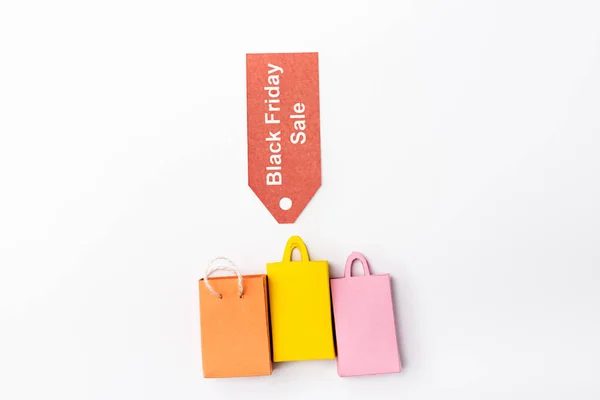 Vue du dessus de l'étiquette de prix avec noir vendredi vente lettrage près de petits sacs à provisions sur fond blanc — Photo de stock