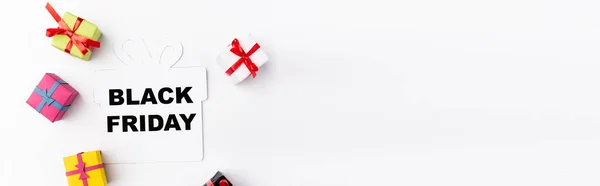 Panoramic shot of paper element with black friday lettering near toy gift boxes on white background — Stock Photo