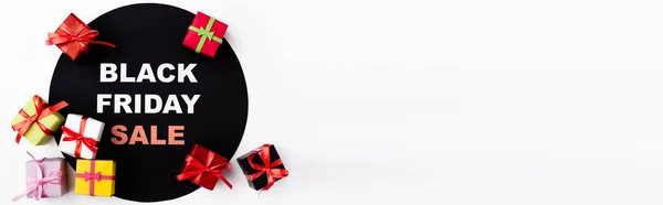 Панорамний знімок чорного кола з чорною п'ятницею з написом та іграшковими подарунковими коробками на білому тлі — стокове фото
