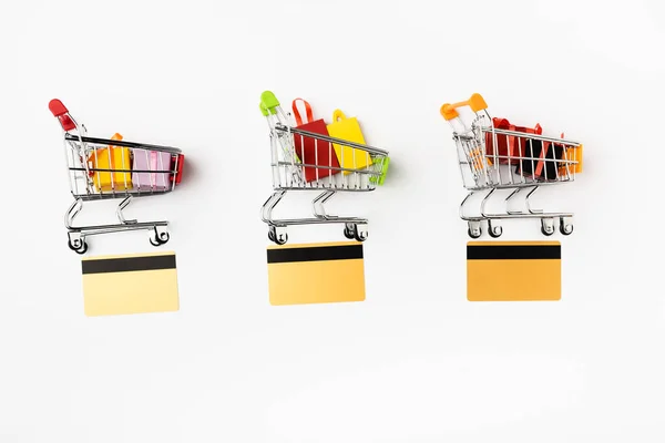 Vista superior de tarjetas de crédito cerca de carritos de compras con regalos de juguete y bolsas sobre fondo blanco - foto de stock