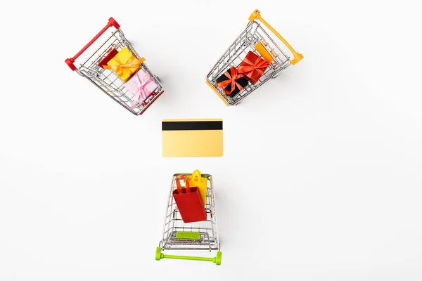 Ansicht von Spielzeug-Einkaufswagen mit Geschenken und Taschen in der Nähe der Kreditkarte auf weißem Hintergrund — Stockfoto