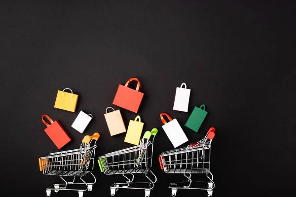 Vista superior de carritos de juguete con coloridas bolsas de compras sobre fondo negro - foto de stock