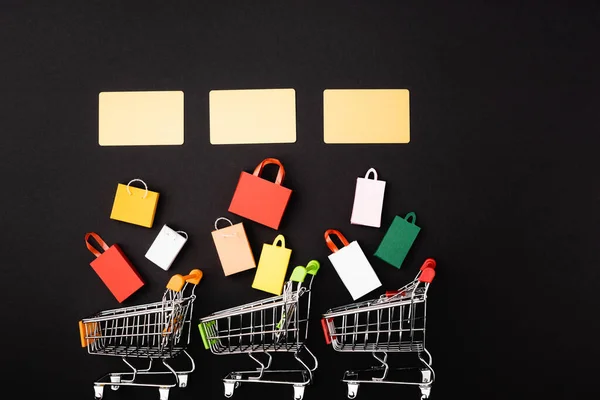 Top view of credit cards near toy shopping bags and carts on black background — Stock Photo