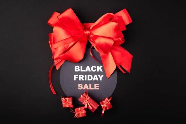 Top view of red bow near circle with black friday sale and small gifts on black background — Stock Photo