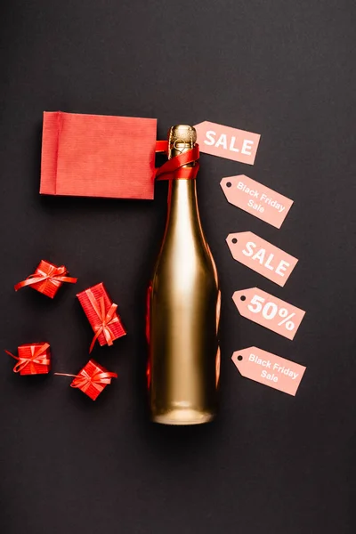 Vista superior de la botella de oro de champán cerca de etiquetas de precio y regalos de juguete sobre fondo negro - foto de stock