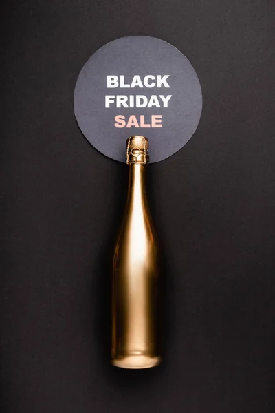 Top view of golden bottle of champagne near circle with black friday sale lettering on black background — Stock Photo