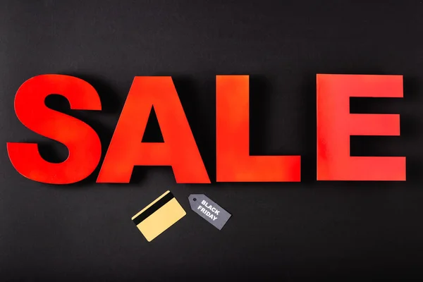 Top view of credit card near price tag and black friday sale lettering on black background — Stock Photo