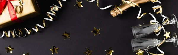 Horizontal crop of bottle of champagne, glasses and gift near decor on black background — Stock Photo