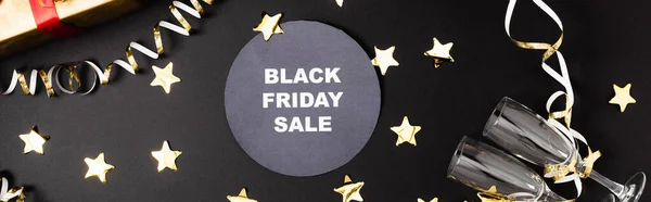 Panoramic shot of round with black friday sale lettering near glasses and decor on black background — Stock Photo