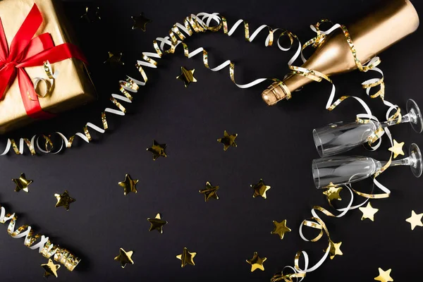 Top view of champagne bottle and glasses near gift box and decor on black background — Stock Photo