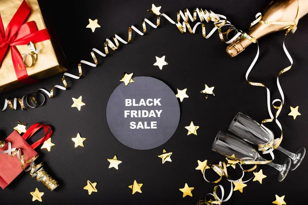 Вид зверху круглий з продажу чорної п'ятниці, що витісняє біля святкового декору, пляшки шампанського та подарунок на чорному тлі — стокове фото