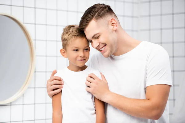 Sorridente papà abbracciando figlio vicino specchio rotondo in bagno — Foto stock