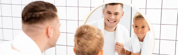 Happy father and son with towels looking at round mirror in bathroom on blurred foreground, banner — Stock Photo