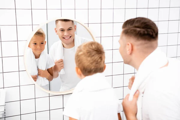 Alegre padre e hijo mirando espejo redondo en el baño en primer plano borroso - foto de stock
