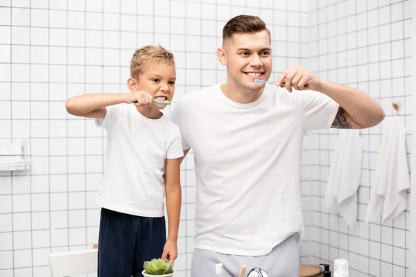 Padre e figlio che mostrano i denti e tengono gli spazzolini da denti, mentre distolgono lo sguardo in bagno — Foto stock