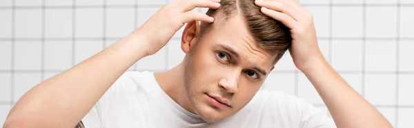 Hombre adulto joven preocupado revisando el pelo en el baño, pancarta - foto de stock
