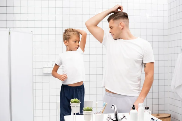 Pai e filho cheirando axilas enquanto em pé perto da pia com produtos de higiene pessoal no banheiro — Fotografia de Stock