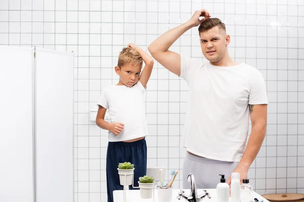 Father and son with armpits smelling badly looking at camera, while standing near sink with toiletries in bathroom — Stock Photo