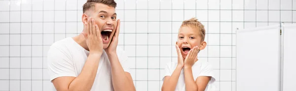 Шокований батько і син кричать, торкаючись щоки руками у ванній кімнаті, банер — стокове фото
