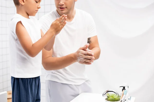 Father and son rubbing soap between hands while standing near sink in bathroom — Stock Photo