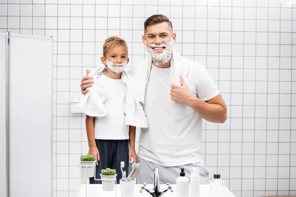 Felice figlio e padre con schiuma da barba sui volti che si abbracciano in bagno — Foto stock