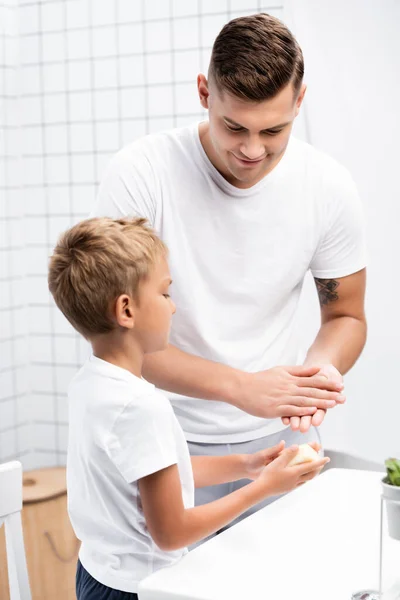 Sorrindo pai lavar as mãos, enquanto olha para o filho com sabão de pé perto pia no banheiro — Fotografia de Stock