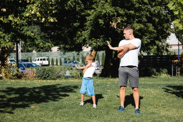 Батько і син у спортивному одязі зігріваються перед тренуванням у парку — стокове фото