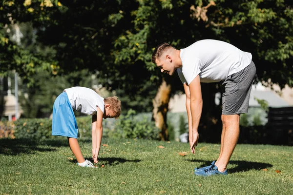 Man and boy in sportswear with outstretched hands, leaning forward in park with blurred trees on background — Stock Photo
