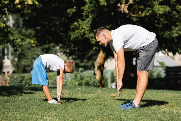 Mann und Junge in Sportkleidung mit ausgestreckten Händen, vorwärts gebeugt im Park mit verschwommenen Bäumen im Hintergrund — Stockfoto