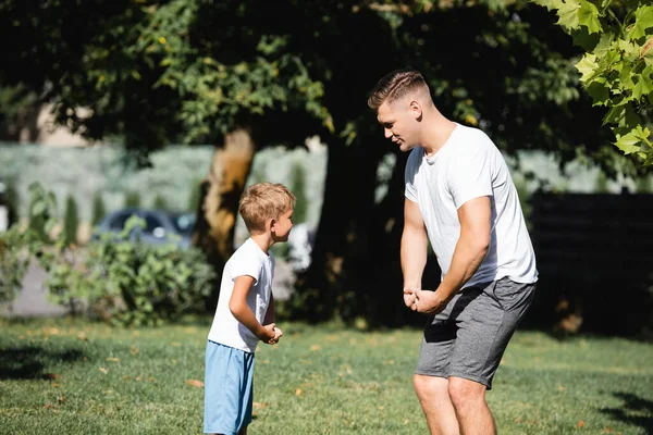 Sohn und Vater in Sportbekleidung zeigen Muskeln im Park auf verschwommenem Hintergrund — Stockfoto